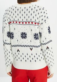 Vitt stickat tröja med ett mönster som har blå snöflingor, röda hjärtan och svarta accenter. Ribbade nacke och ärmslut.