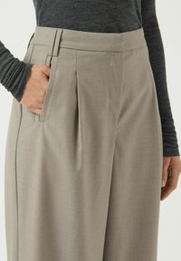 Beige geplooide broeken van gladde stof, met een platte voorkant, zijzakken en een getailleerde pasvorm bij de taille.