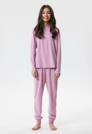 Fille debout pieds nus portant un pyjama rayé rose et blanc à manches longues avec un pantalon assorti, souriant à la caméra.