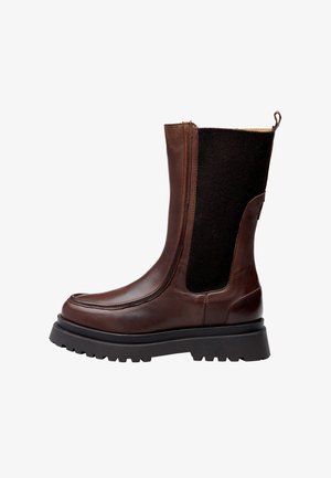 Botte de cheville en cuir marron avec des panneaux élastiques noirs, surface texturée, bout rond et semelle en caoutchouc épaisse. Fermeture éclair sur le côté pour un enfilage facile.