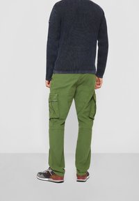 Gröna cargobyxor med sidofickor och smal passform, ihop med en mörk, texturerad tröja och flerfärgade sneakers.