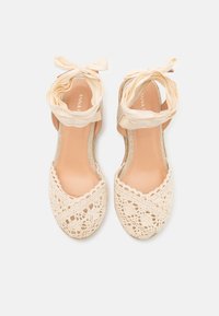 Bottines espadrilles en crochet beige avec une fine sangle en tissu. Bout rond et semelle plate, arborant un motif texturé semblable à de la dentelle.