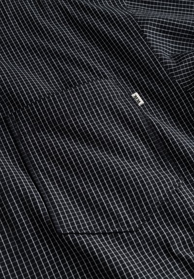 Detalje af sort-hvid ternet skjorte med en lappelomme og et lille mærke, med en glat stoftekstur og et rutemønster.