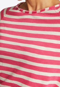 Top en coton rayé rose et blanc avec un large col et des bords effilochés. Présente une coupe décontractée et une texture douce.