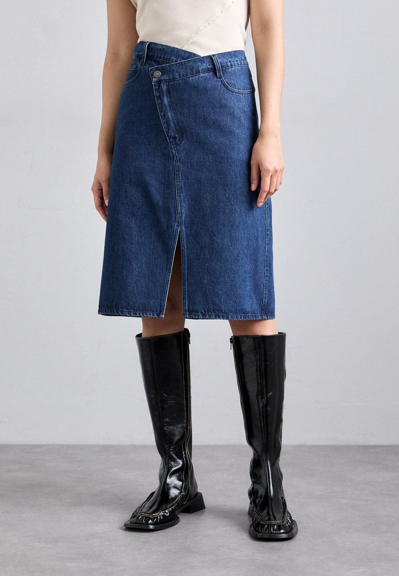 Denim A formos sijonas su priekiniais plyšiais, tamsiai mėlynos spalvos, su sagčių uždarymu. Derinamas su juodomis blizgiomis iki kelių ilgio botais.