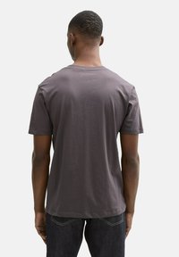 Tricou gri din bumbac, cu mâneci scurte, guler rotund și o croială lejeră. Materialul pare moale și ușor, având o textură fină.