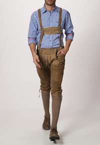 Pantalones de cuero marrón con costuras decorativas, combinados con una camisa a cuadros azul y blanco. Zapatos marrones y calcetas marrones hasta la rodilla completan el atuendo.