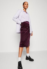 Violeta samta midi svārki ar sānu plaisu, apvienoti ar gaiši violetu pogājamā krekla un melniem platformas loafers ar baltām zeķēm.