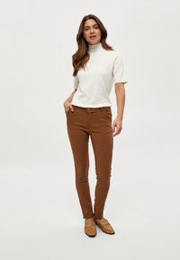 Top blanco de manga corta con cuello alto combinado con pantalones marrones ajustados y mocasines color beige, con un diseño simple y sin patrones visibles.
