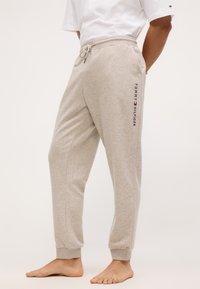 Pantaloni de trening gri deschis, confecționați dintr-un material moale, cu talie ajustabilă prin șnur și manșete ribbate; logo-ul "Tommy Hilfiger" imprimat în nuanțe de bleumarin pe lateral.
