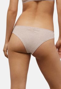 Bragas bikini de algodón beige con textura suave, tiro bajo y detalles sutiles de costura trasera. Diseño sencillo, sin logotipos o patrones visibles.