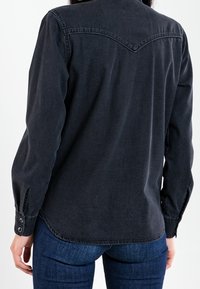 Black denim shirt with a pointed yoke, long sleeves, buttoned cuffs, and a slightly curved hem. Texture appears smooth with minor fading.