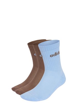 Trzy pary prążkowanych skarpetek za kostkę, dwie pary brązowe i jedna jasnoniebieska, każda z logo Adidas blisko kostki.