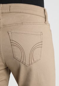 Närbild av beige byxor med böjd dekorativ sömnad på bakfickan, som används över en svart topp.