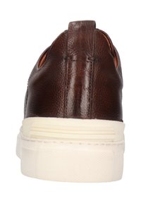 Zapato marrón de cuero tipo slip-on con una superficie texturizada, que cuenta con una suela de goma blanca y sutiles recortes laterales.