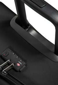 Valigia nera con ruote, superficie in nylon texturizzato, maniglia telescopica e lucchetto a combinazione TSA sulla cerniera.