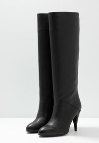 Černé kožené vysoké boty po kolena s špičatou špičkou a jehlovým podpatkem. Hladká textura s přiléhavým designem a minimálními švy.