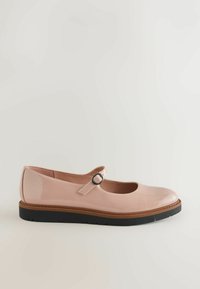 Une chaussure Mary Jane en cuir verni rose pâle avec une bride à boucle noire et une semelle noire épaisse vue de profil.