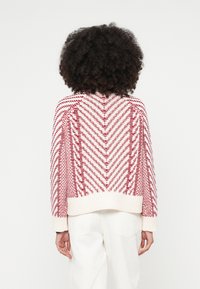 Πλεκτό πουλόβερ με σχέδιο σε σχήμα ζιγκ-ζαγκ σε κόκκινο και λευκό, με ριμπ στη βάση και στα μανίκια, χαλαρή γραμμή και μαλακή υφή.