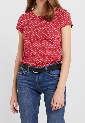 Kobieta nosząca czerwony krótki rękaw z wzorem w zygzak, wsunięta w niebieskie dżinsy z czarnym paskiem.