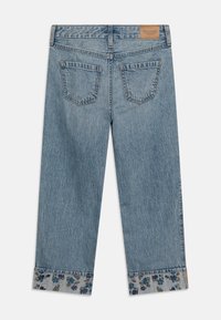 Jean en denim bleu clair avec une coupe droite, ornés d'une broderie florale aux poignets et d'une étiquette beige sur la taille arrière.