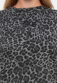 Dettaglio ravvicinato di un tessuto grigio con stampa leopardo e logo "GAP" ricamato in nero nella parte superiore del petto.