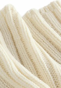 Tissu tricoté couleur crème avec une texture côtelée. Fil épais avec des coutures visibles, présentant des fibres douces et chaudes.
