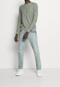 Suéter gris de manga larga hecho de tela de punto, combinado con jeans ajustados de color azul claro y zapatillas blancas. Diseño simple sin estampados.