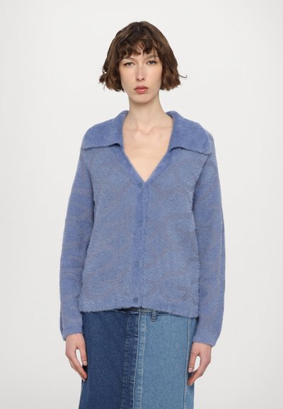 Cardigan en peluche bleu avec un col, un motif texturé et une fermeture à boutons, associé à une jupe en denim.