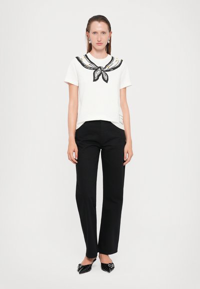 Tricou alb cu guler decorativ negru și galben, asortat cu pantaloni negri drepti și pantofi negri cu vârf ascuțit, împodobiți.