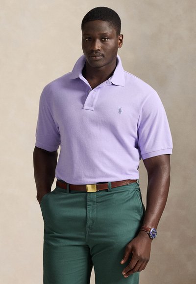 Μωβ polo μπλούζα με ριγέ γιακά και κεντημένο λογότυπο, συνδυασμένη με πράσινα παντελόνια και καφέ ζώνη με ασημένια πόρπη.