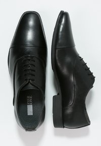 Chaussures habillées en cuir noir avec une finition lisse, présentant un bout pointu, un laçage sur le devant et un petit talon bloc. Accentué par un design cousu.