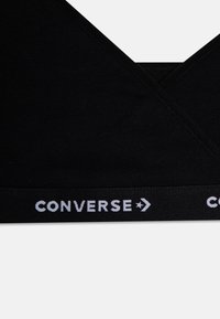 Fekete pamut melltartó V-kivágással. Széles elasztikus pánttal rendelkezik, fehér "CONVERSE" logóval és nyíldetáldokkal. Puha textúra.