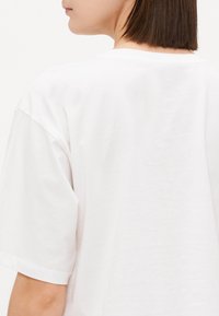 Hvit bomulls t-skjorte med rund hals og korte ermer, sett fra bak. Stoffet er glatt med en lett glans.