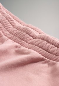 Rosa tyg med mjuk textur, med gummidetaljer som är samlade längs ena kanten. Nærtitt som framhäver sömmarna och materialets kvalitet.