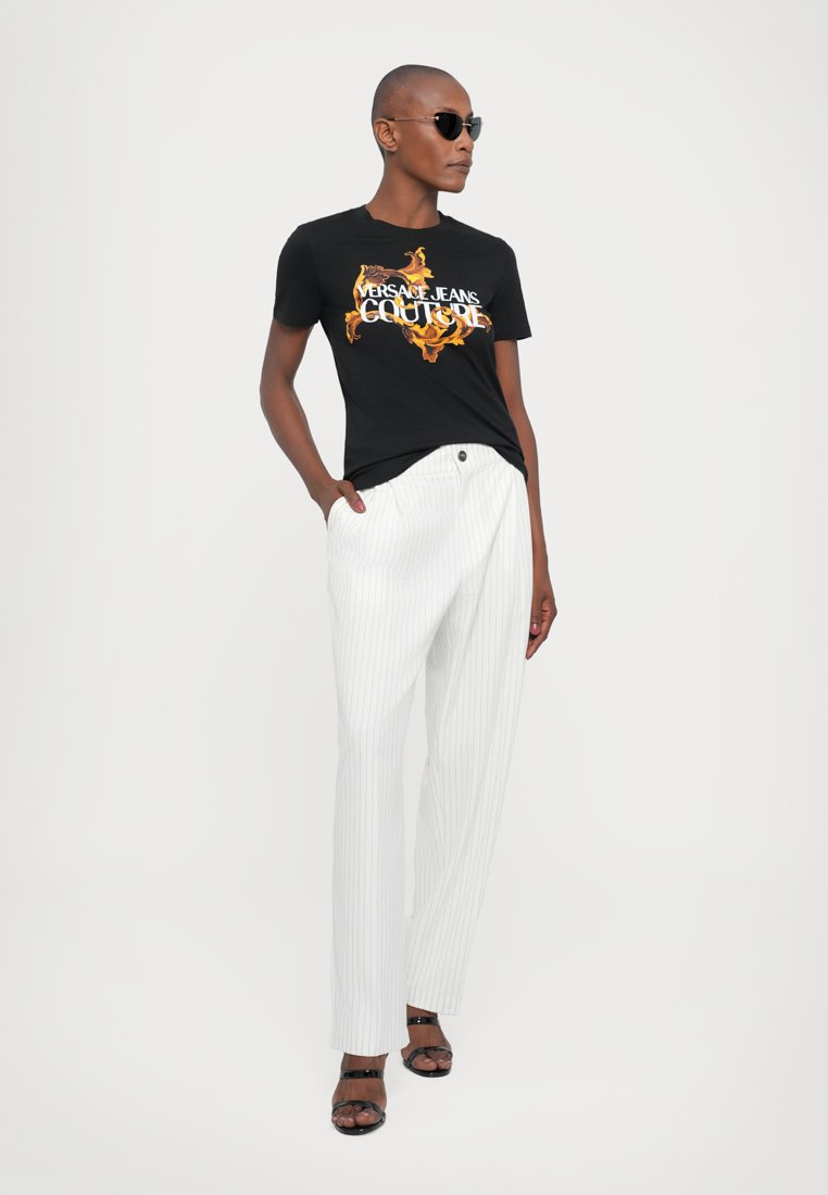 T-shirt en coton noir avec un imprimé graphique coloré, associé à un pantalon blanc à rayures et des sandales noires au design épuré.