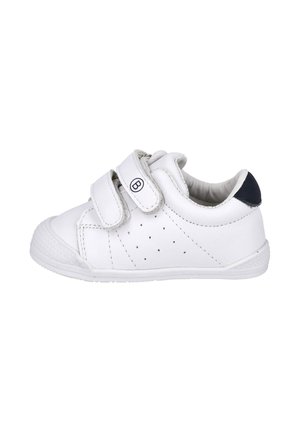 Zapatilla blanca para niño pequeño con dos tiras de velcro, pequeñas perforaciones en el lateral y acento oscuro en el talón, mostrada de perfil sobre fondo blanco.