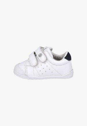 Zapatilla blanca para niño pequeño con dos tiras de velcro, pequeñas perforaciones en el lateral y acento oscuro en el talón, mostrada de perfil sobre fondo blanco.