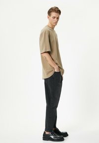 Camiseta de algodón beige con un ajuste relajado, combinada con jeans negros ajustados y zapatos negros. Textura suave, diseño simple, sin patrones visibles.