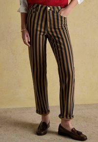 Pantaloni din denim cu dungi maro și bleumarin, cu talie înaltă, tivuri rulotate și design clasic cu cinci buzunare. Purtați cu pantofi loafer maro.