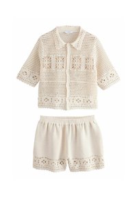 Ensemble deux pièces de couleur crème avec finition en dentelle, comprenant un haut à manches courtes avec boutons et un short assorti ornés de motifs découpés complexes.