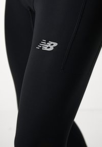 Close-up of black athletic leggings with a reflective New Balance logo on the upper thigh.
