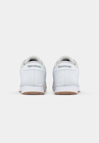Sapatilhas brancas com um cabedal de couro liso, forro cinza suave e uma sola de borracha de cor contraste. Apresenta o logótipo da Reebok no calcanhar.