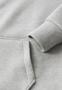 Lys grå sweatshirtstof med en glat tekstur, der har en manchet og en søm til frontlommen. Enkel design, uden mønstre eller hardware.