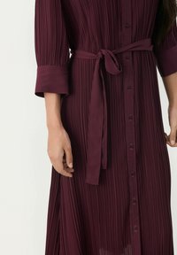 Burgundy pleated dress with a button-down front, three-quarter sleeves, and a tied waist belt, made from lightweight fabric.