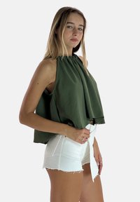 Top halter verde realizzato in tessuto leggero, caratterizzato da una vestibilità ampia e una scollatura arricciata, abbinato a pantaloni corti bianchi in denim a vita alta.