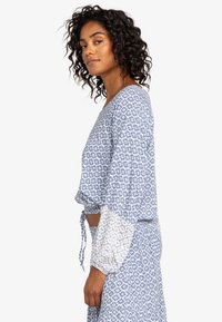 Blauw patroon top met lange mouwen, voorzien van een strikdetail in de taille en een contrasterende bloemenprint op de mouwen. Lichtgewicht stof.