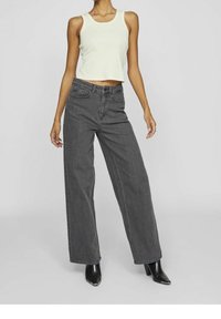 Zkrácený světle zelený top na ramínka, kombinovaný s volnými tmavě šedými d�žíny s vysokým pasem a černými kotníkovými botami na podpatku. Hladká textura látky.