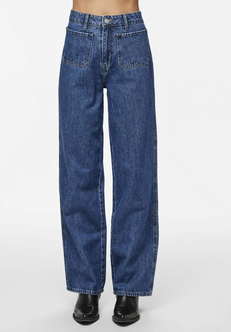 Jeans in denim blu a gamba larga con due tasche frontali, un'alta vita e chiusura a bottoni, abbinati a stivali neri alla caviglia.