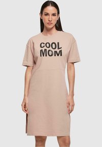 Svetloružové bavlnené šaty vo forme trička s krátkymi rukávmi, na ktorých je v tučnom čiernom písme nápis "COOL MOM". Po stranách sú rozparky na leme.